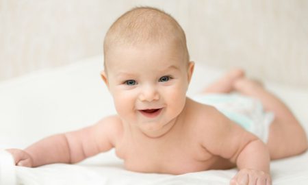 Funny infant baby at home, holds head up, put on a tummy on a white blanket. Family, baby development concept photo